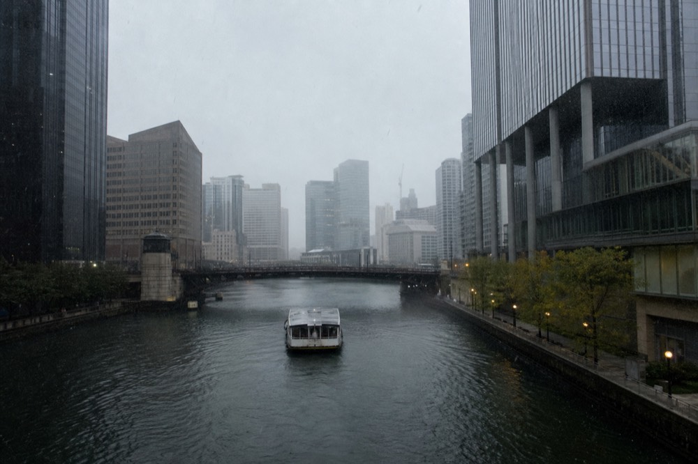 A Chicago architecture cruise boat moving down the river under gray skies with skyscrapers rising on both banks, no text, no logos, no people.