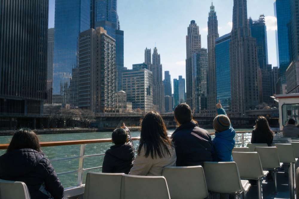 A family with children pointing at Chicago skyscrapers from the open deck of a river cruise boat, no text, no logos, no people