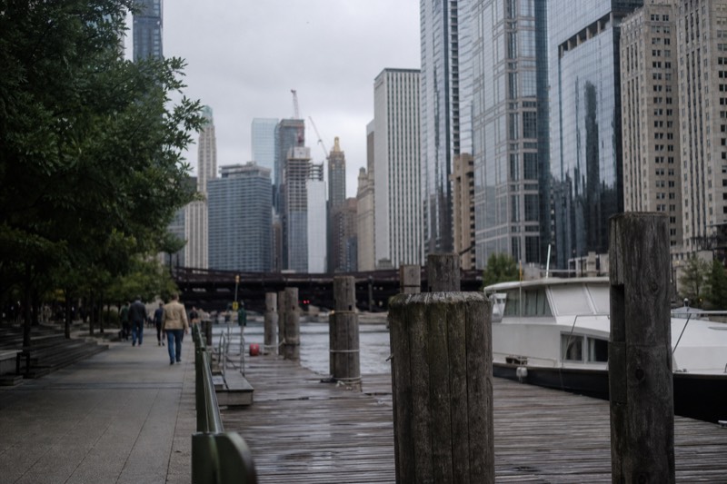Chicago Riverwalk-promenaden i blødt morgenlys, med en træbro i forgrunden og byens horisont bagved
