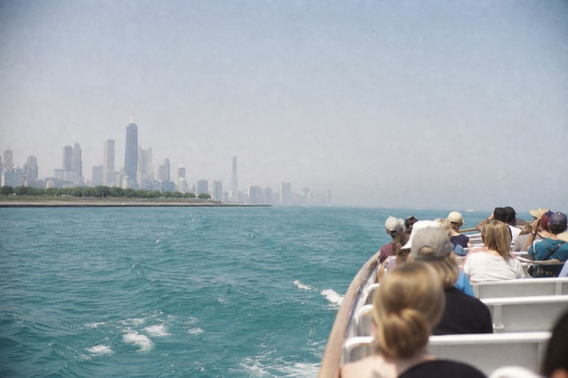 En tursejlads lige forbi molen ved flodmundingen med åbent Lake Michigan-vand forude og byens horisont, der fjerner sig bagved
