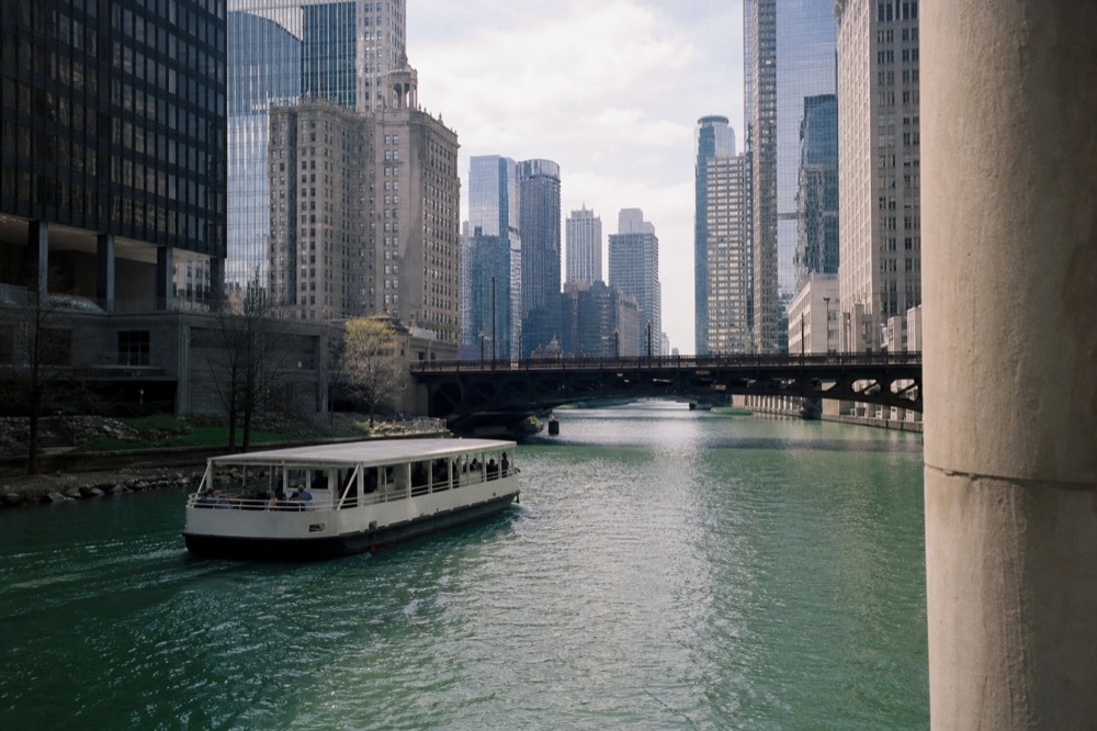 Downtown Chicago buildings reflected in green river water with a tour boat passing under a bascule bridge, no text, no logos, no people.